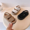 A pair of beige soft-soled sandals for toddlers is shown on a light surface.