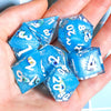 A hand holds a set of blue resin polyhedral dice with various numbers and symbols.