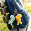 A yellow crochet dinosaur keychain is attached to a denim jean pocket resting on a wooden bench.