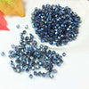 A pile of dark blue faceted crystal beads is displayed on a white surface next to some colored leaves.