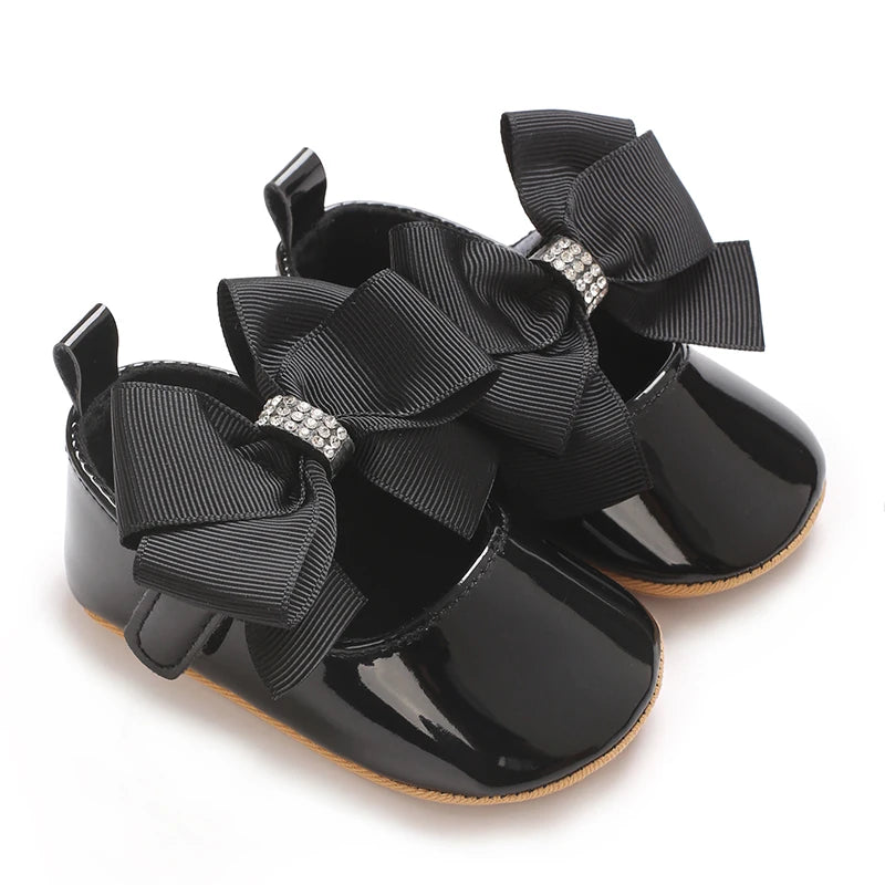 Black moccasin shoes for a baby girl featuring a black ribbon bow with silver lace trim