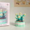 A miniature flower bouquet made of light blue and cream building blocks displayed next to its packaging.