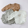 A collection of three embroidered cotton baby rompers in beige, gray, and white.