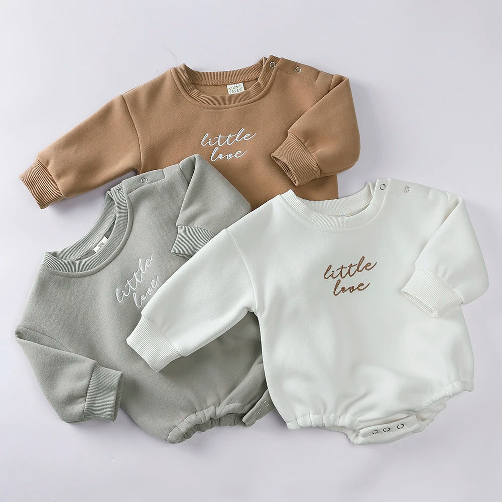 A collection of three embroidered cotton baby rompers in beige, gray, and white.