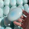 A hand holds a light blue cheese-shaped squishy stress relief toy surrounded by many similar toys.
