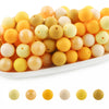 A variety of round silicone beads in shades of yellow, orange, and cream are displayed on a white surface.