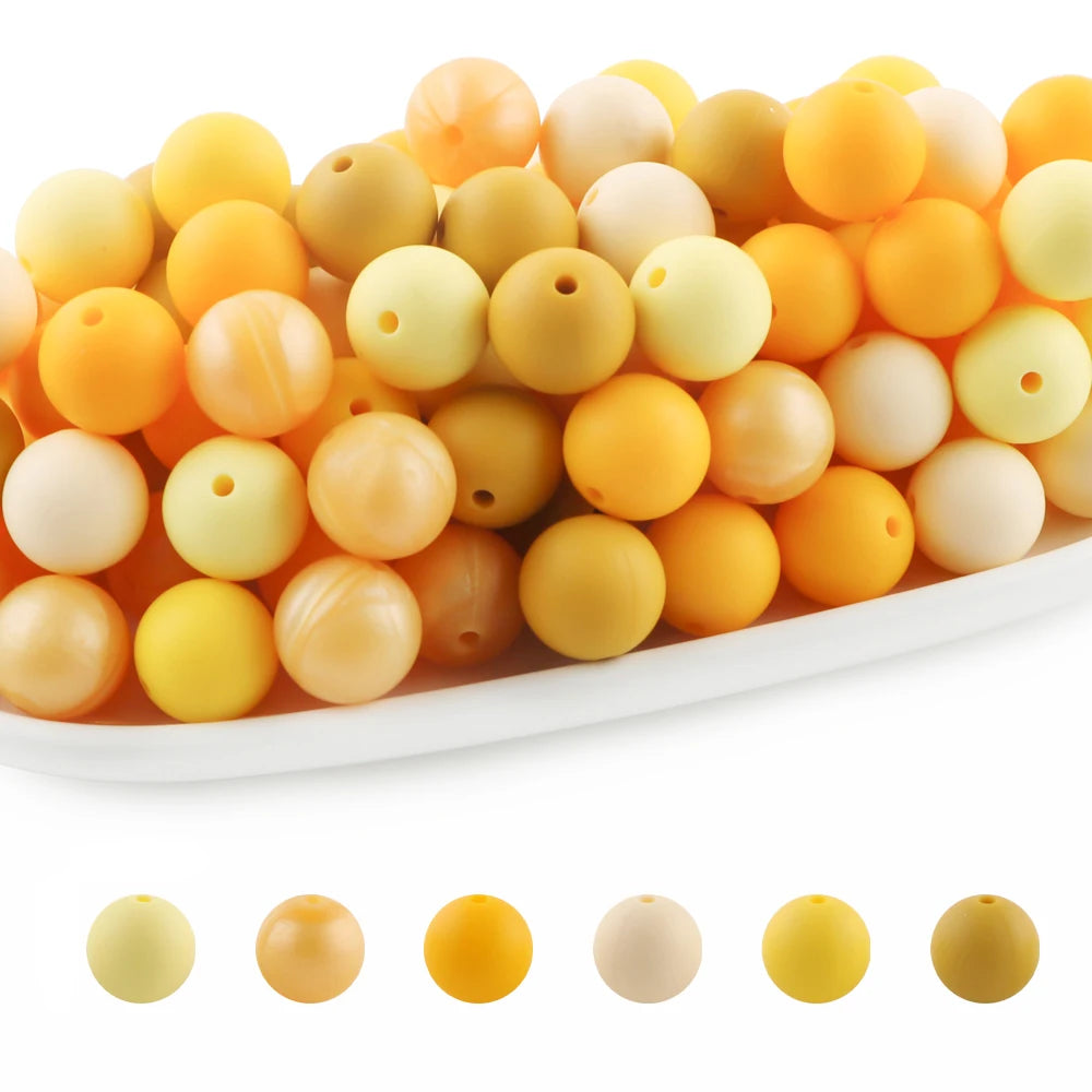 A variety of round silicone beads in shades of yellow, orange, and cream are displayed on a white surface.