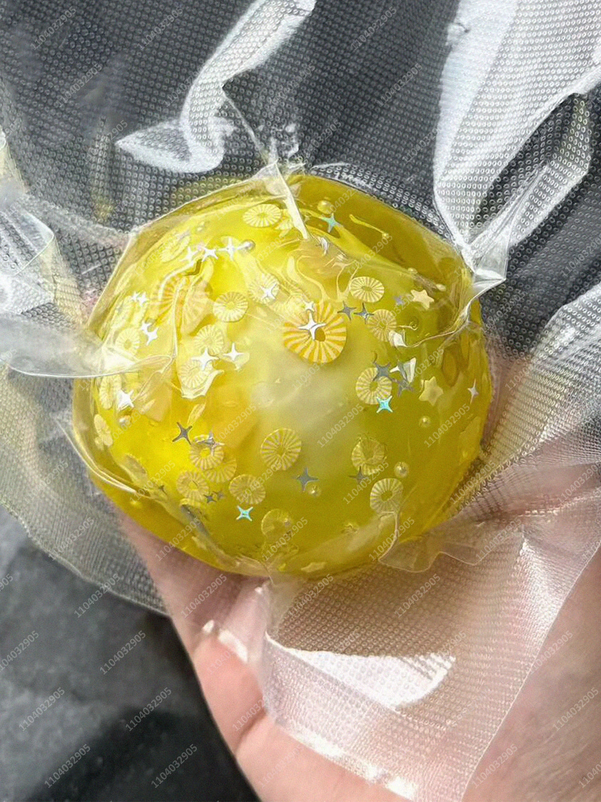 A yellow stress ball filled with small, shiny, gold-colored objects is wrapped in clear plastic.