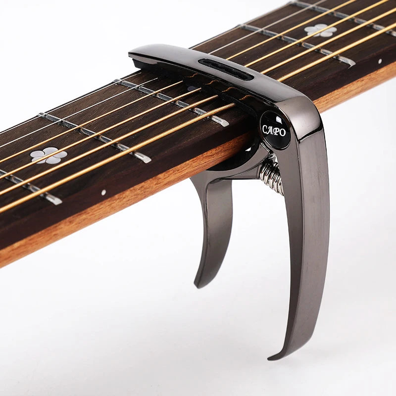 A close-up view of a professional metal guitar capo with a pick holder mounted on the fretboard.