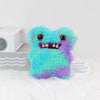A fluffy, bright blue and purple monster plush toy with large eyes and a toothy grin.