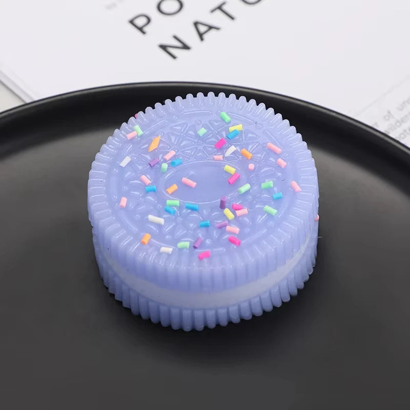 A purple biscuit squishy stress relief toy with colorful sprinkles resting on a dark gray plate.