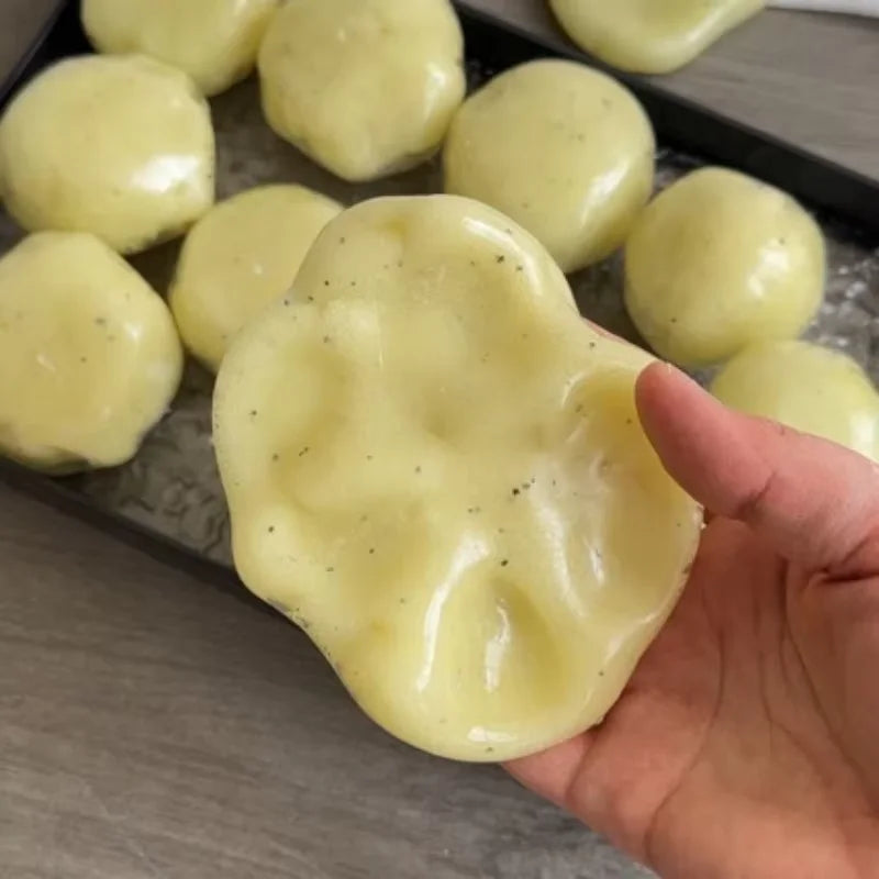 A hand is squeezing a pale yellow mashed potato squeeze toy stress reliever against a dark tray.