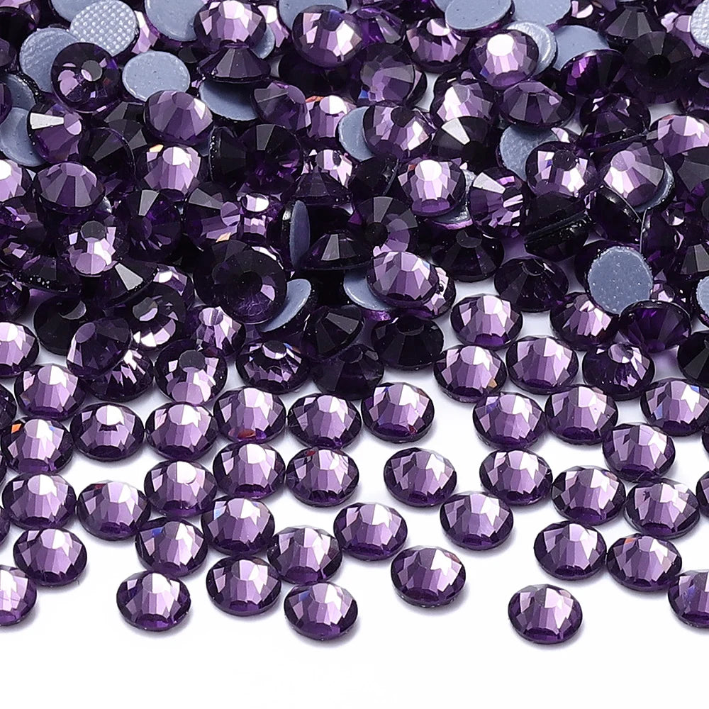 A close-up view of purple and dark violet glass crystal hot fix rhinestones scattered on a white surface.