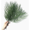 A hand holds a vibrant green artificial tropical palm and monstera leaf arrangement.