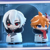 Two chibi figurines of Fatui Harbingers, one white-haired and one orange-haired, displayed in a framed box.