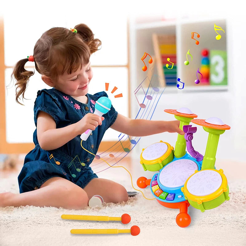 A young girl plays an interactive kids drum set with light-up pads and a microphone on a soft surface.