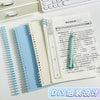 A spiral notebook with a light blue cover and white pages is shown next to a white keyboard and a pencil.