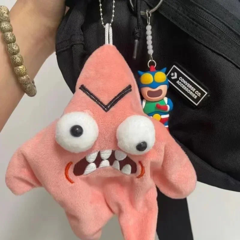 A pink plush toy shaped like a starfish with large eyes and a black facial expression attached to a keychain.