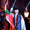 A man wearing a Palestinian flag draped over his shoulder, looking towards the camera on a stage.