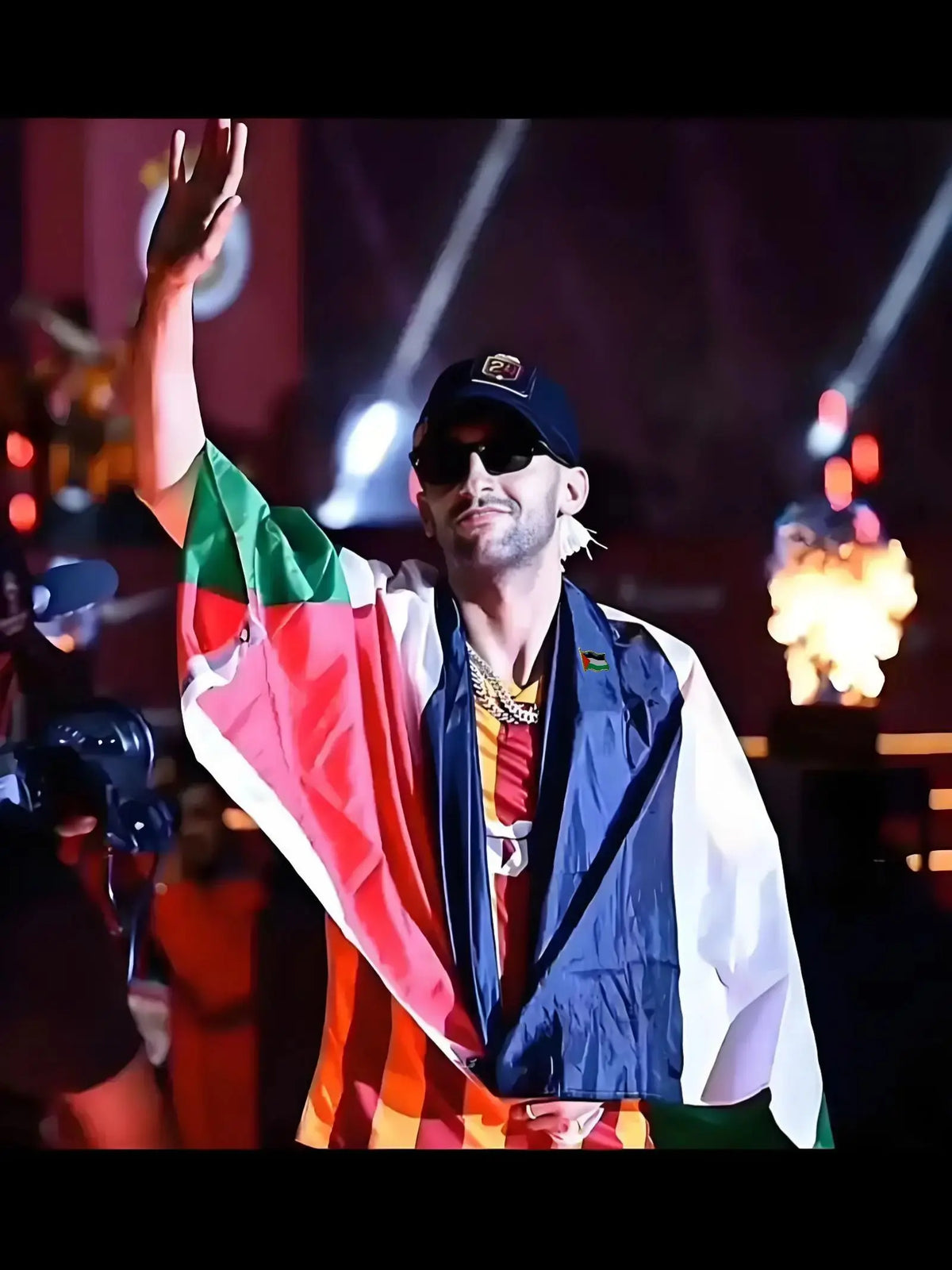A man wearing a Palestinian flag draped over his shoulder, looking towards the camera on a stage.