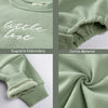 Close-up of a sage green embroidered cotton garment showing the phrase little love and fabric texture.