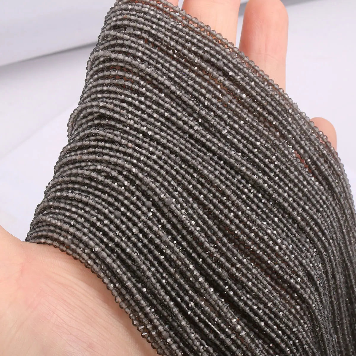 A close-up of dark gray faceted natural stone beads threaded onto a string, shown on a hand.