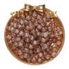 A round gold-rimmed dish filled with small, reddish-brown glass crackle beads for jewelry making.