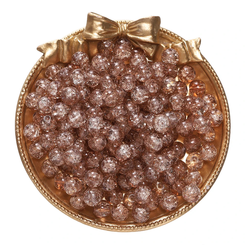 A round gold-rimmed dish filled with small, reddish-brown glass crackle beads for jewelry making.