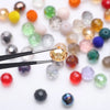 A pair of tweezers is picking up a faceted, golden-yellow crystal bead from a scattered collection of colorful glass beads.