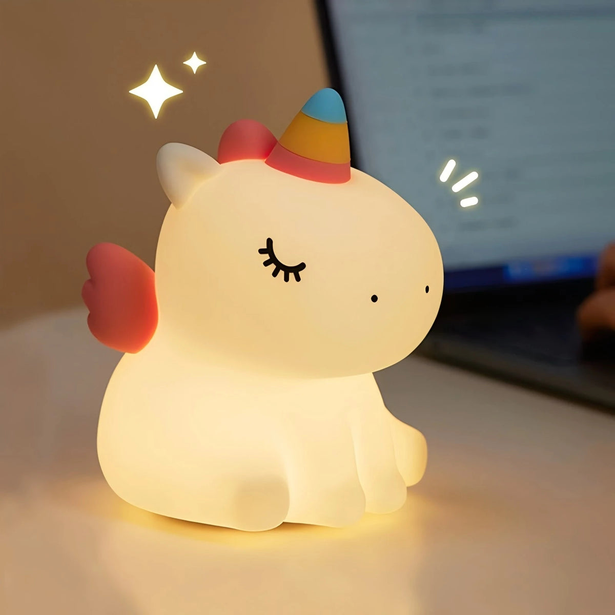 A cute silicone rabbit night light with a pink and orange conical hat is illuminated on a desk.