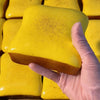 A hand in a pink glove holds a bright yellow, squishy cube toy.