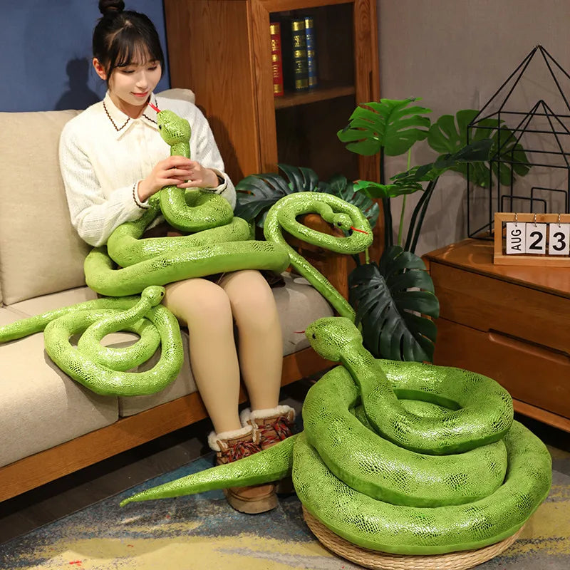 A bright green realistic giant snake plush toy is displayed on a wooden surface.