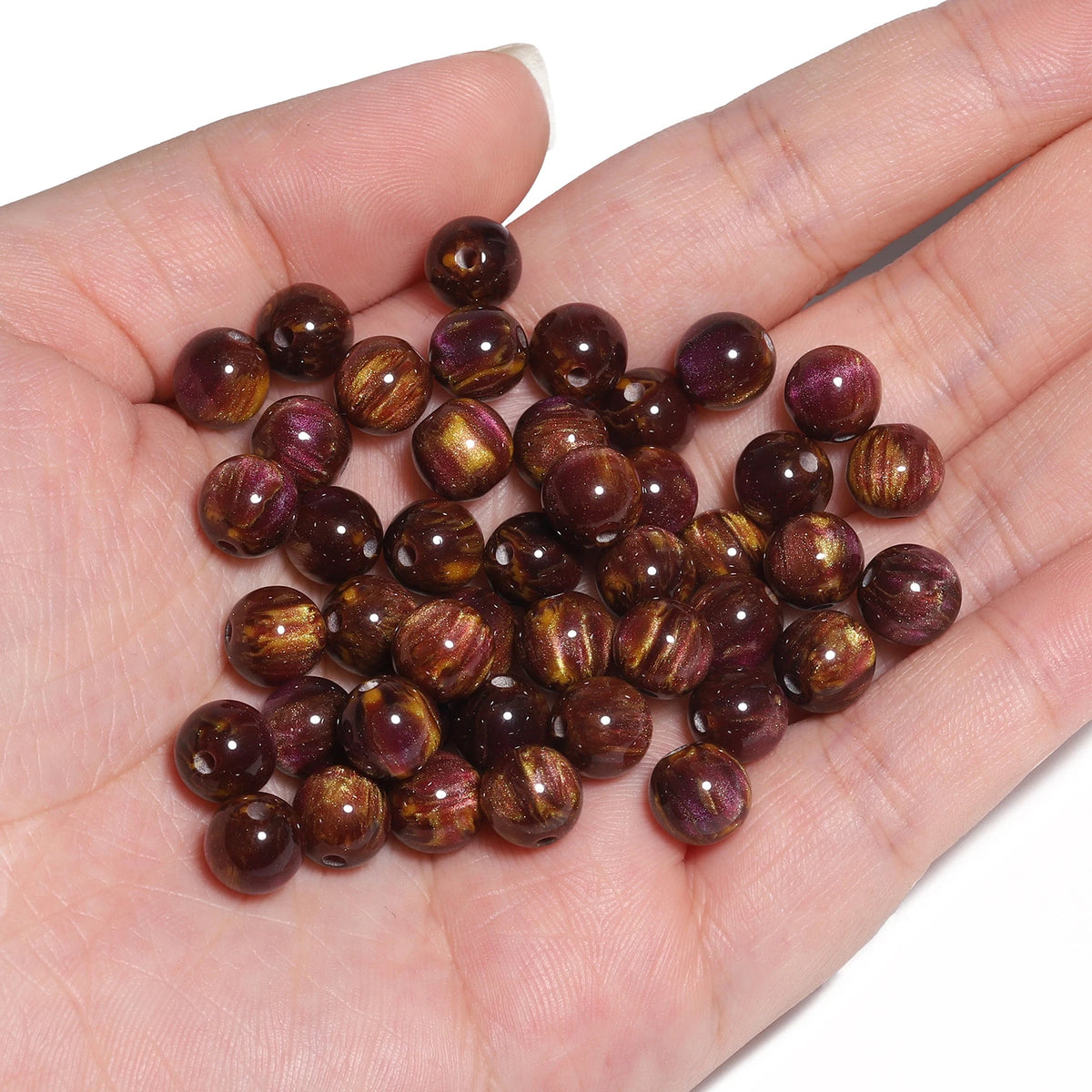 A hand holds a set of 50 vibrant tiger eye resin beads for jewelry making.