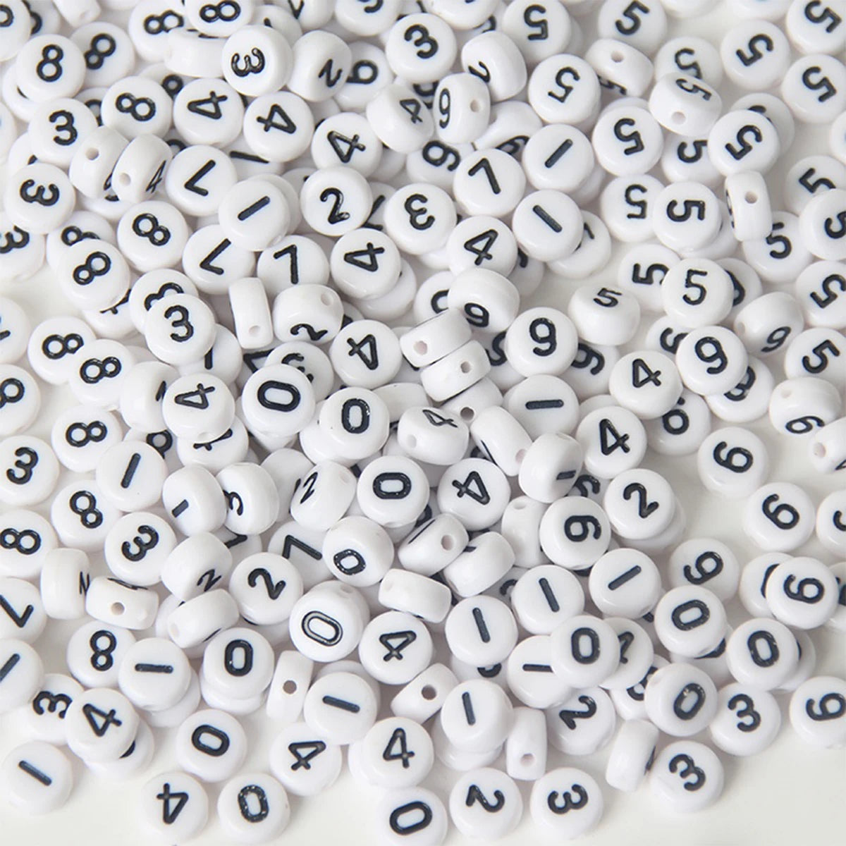 A pile of small white acrylic number beads with black numbers scattered on a white surface.