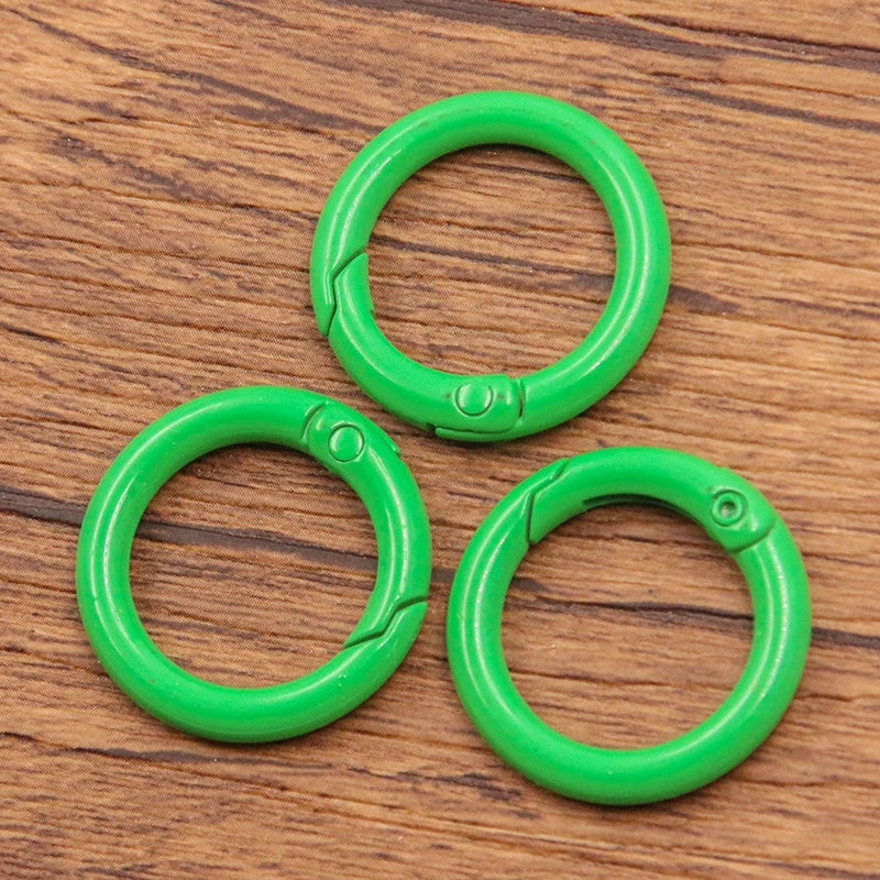 A set of four bright green metal O-ring spring clasps for DIY jewelry and keychains resting on a wooden surface.