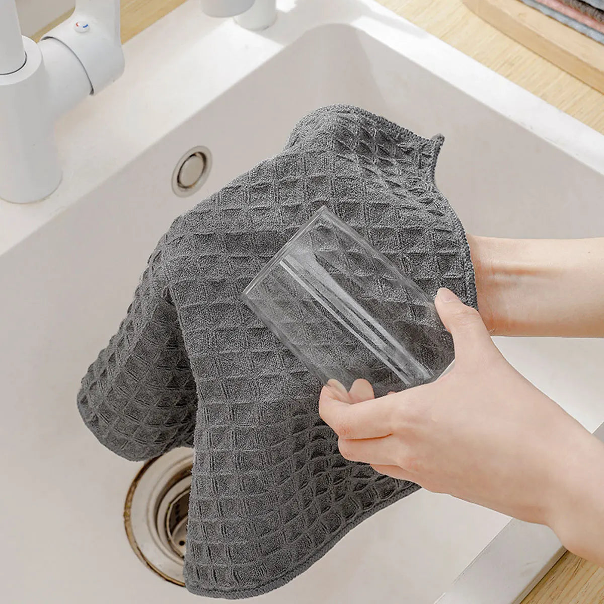 A hand is holding a gray microfiber kitchen cleaning cloth over a white sink basin.