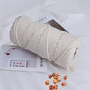 A tightly wound beige natural cotton macrame rope is shown next to a small box of red beads and other craft materials.