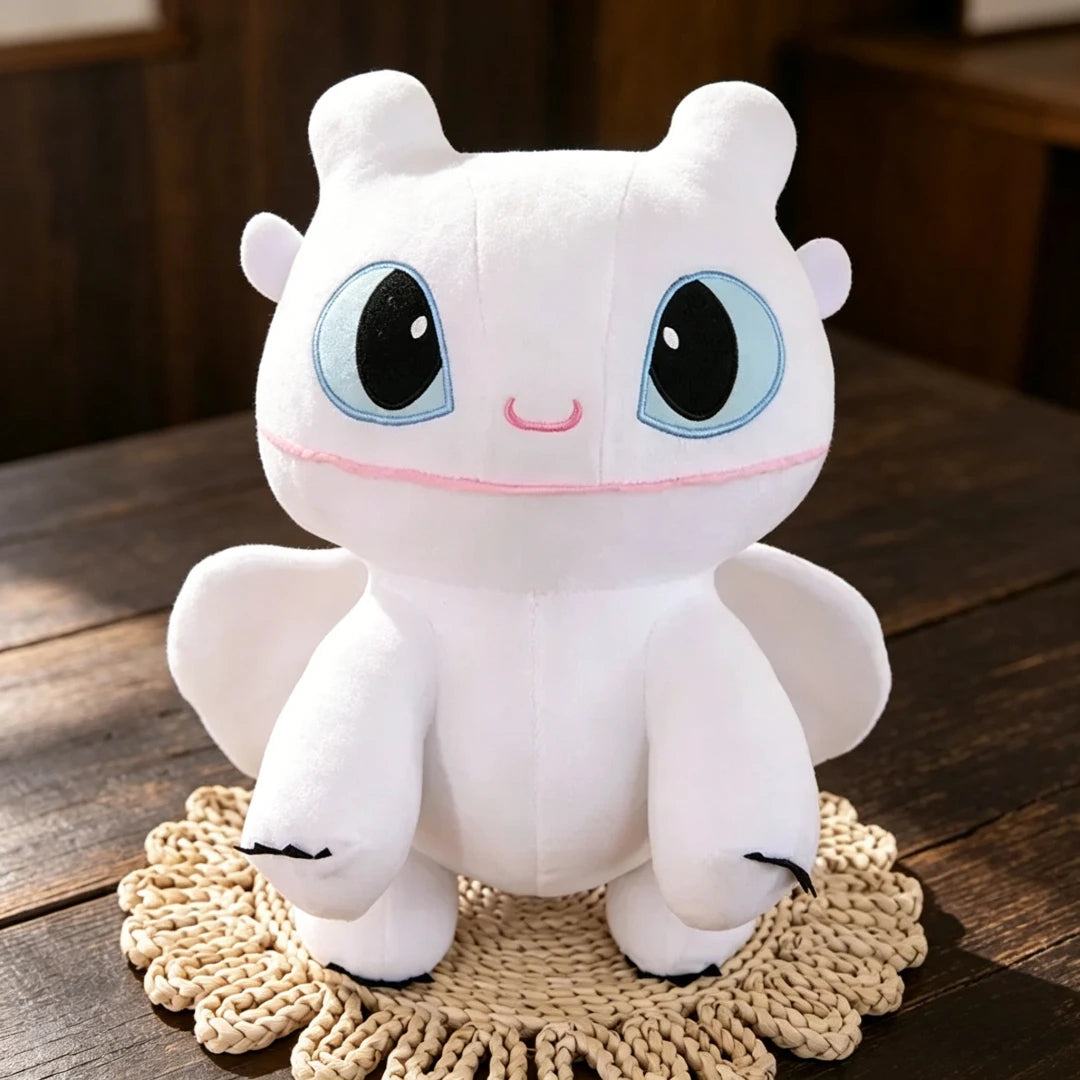 A white cartoon plush dragon with large blue eyes and pink accents sitting on a woven mat.