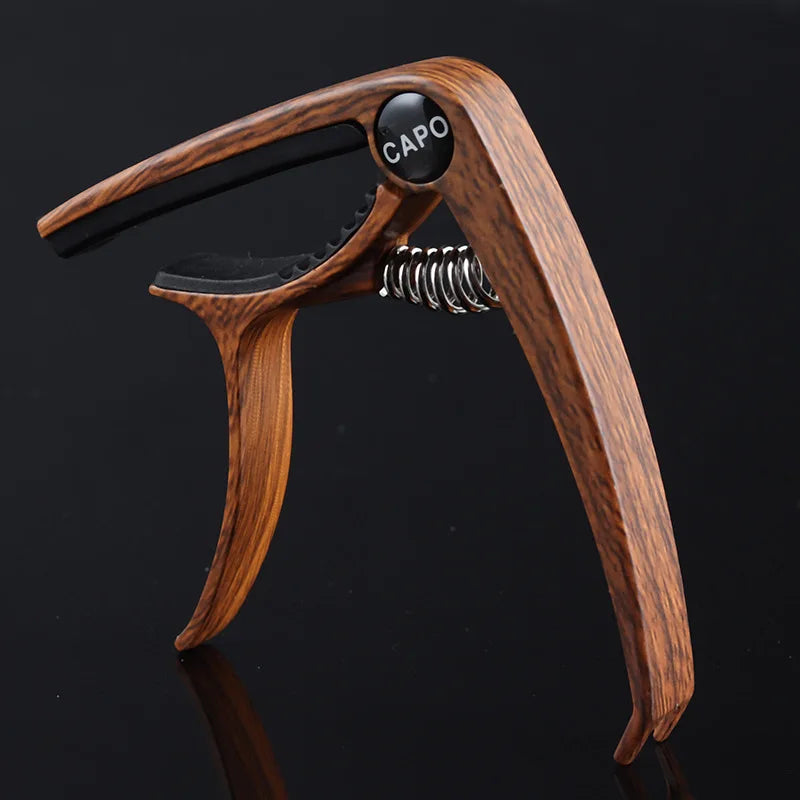 A wooden capo with a black cap and silver spring mechanism shown against a dark background.