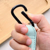 A hand holds a black, curved organizer hook attached to a light green PU leather strap.