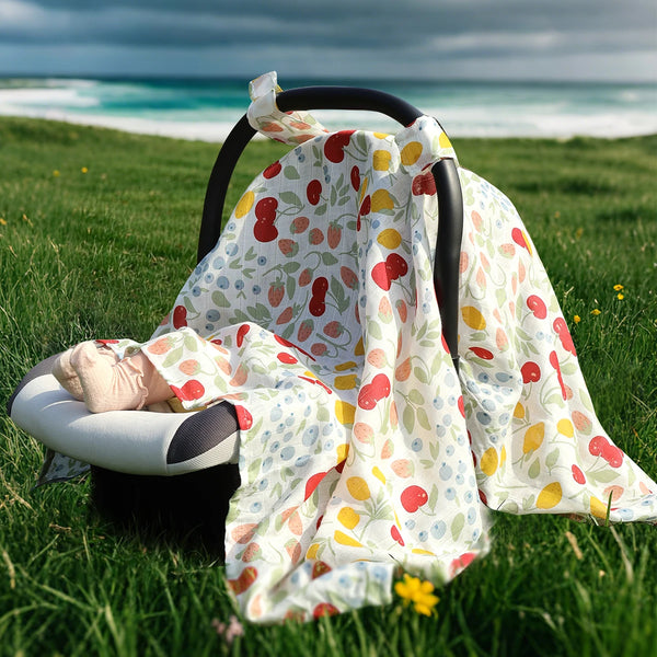 A natural bamboo and cotton baby sunshade car seat cover draped over a black car seat in a grassy field near the ocean.