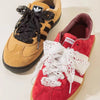 A pair of red suede Adidas sneakers with white lace detailing and black fabric laces.