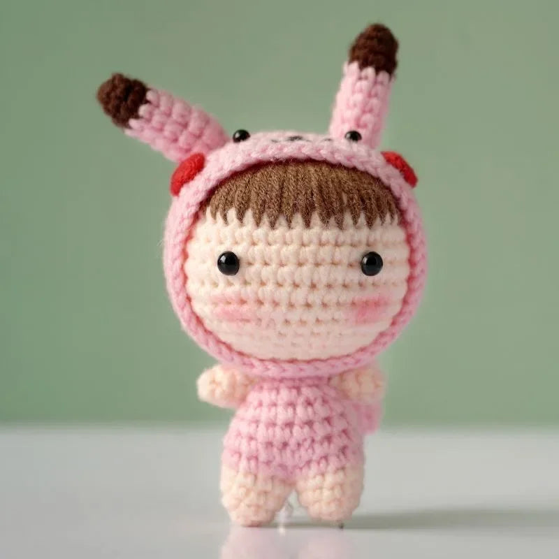 A handmade crochet doll kit featuring a pink body, face, and brown hair with pink ears.