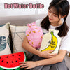 A woman holds a pink and yellow portable hot water bottle with a fruit design against a sofa background.
