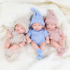 Three realistic soft vinyl baby dolls wearing knitted outfits lying on a white fluffy blanket