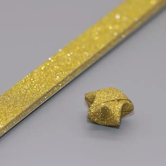 A gold glitter paper strip is shown alongside a folded origami star shape.