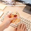 A hand holds a transparent glitter capybara slow-rising squishy toy on a laptop keyboard.