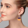 A close-up of a woman's ear showing an orange pudding-shaped resin pendant earring.