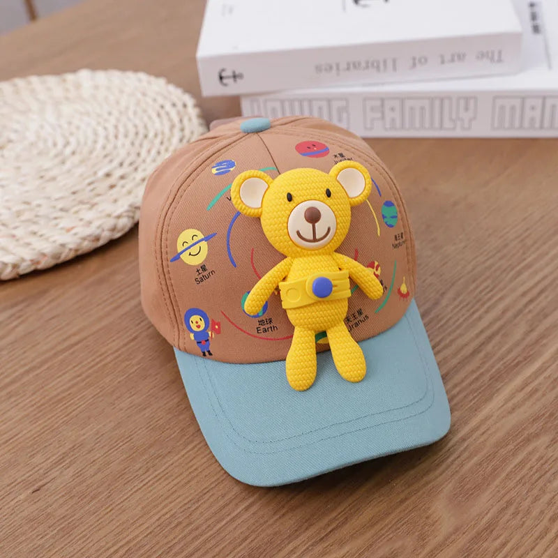 A yellow bear baseball cap featuring a 3D design, resting on a wooden surface next to some books.