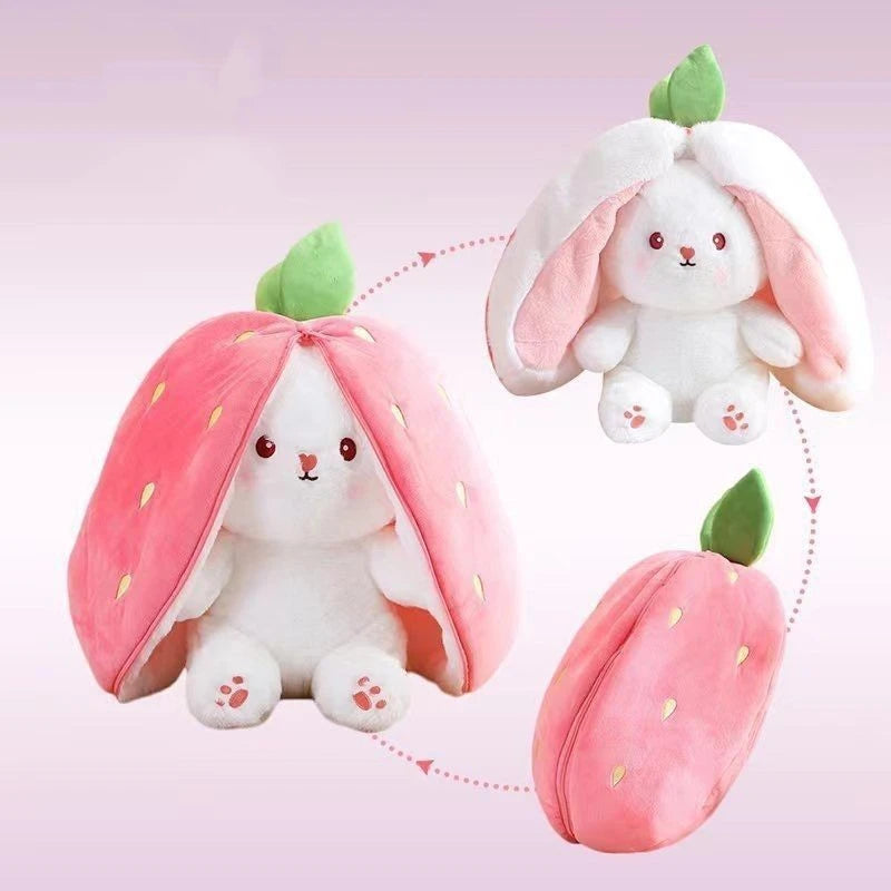 A white bunny plush toy peeking out from a pink strawberry shaped fabric, with a separate strawberry plush nearby.